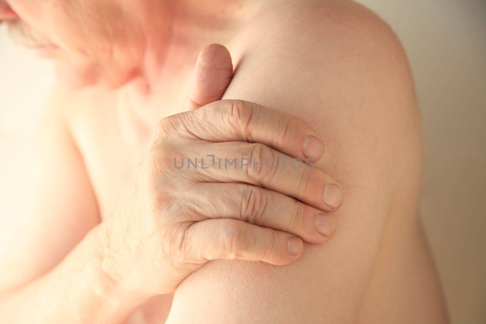 An older man with his hand on an area of soreness on his upper arm