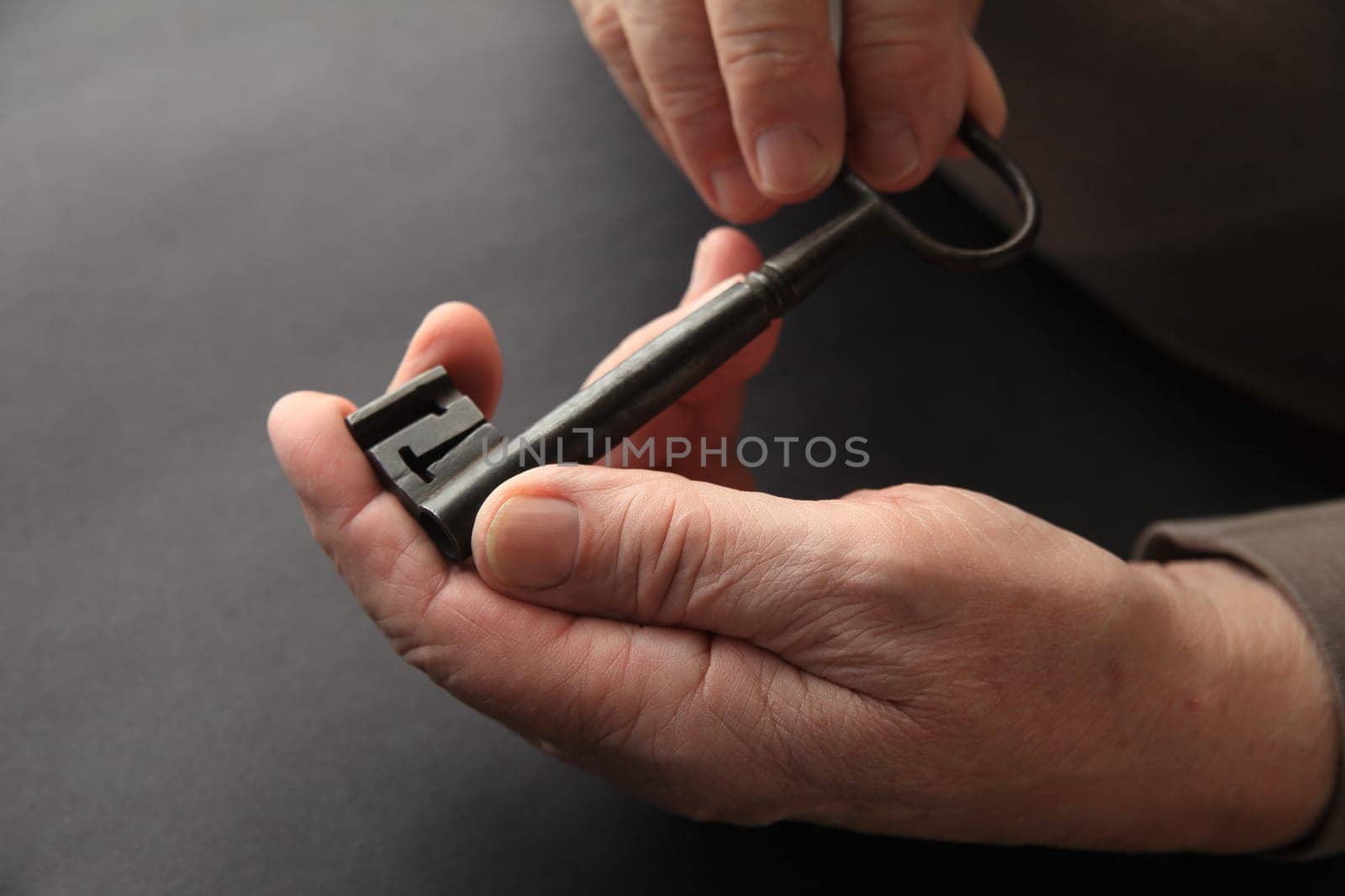 An older man holds a large, antique key on a black background.