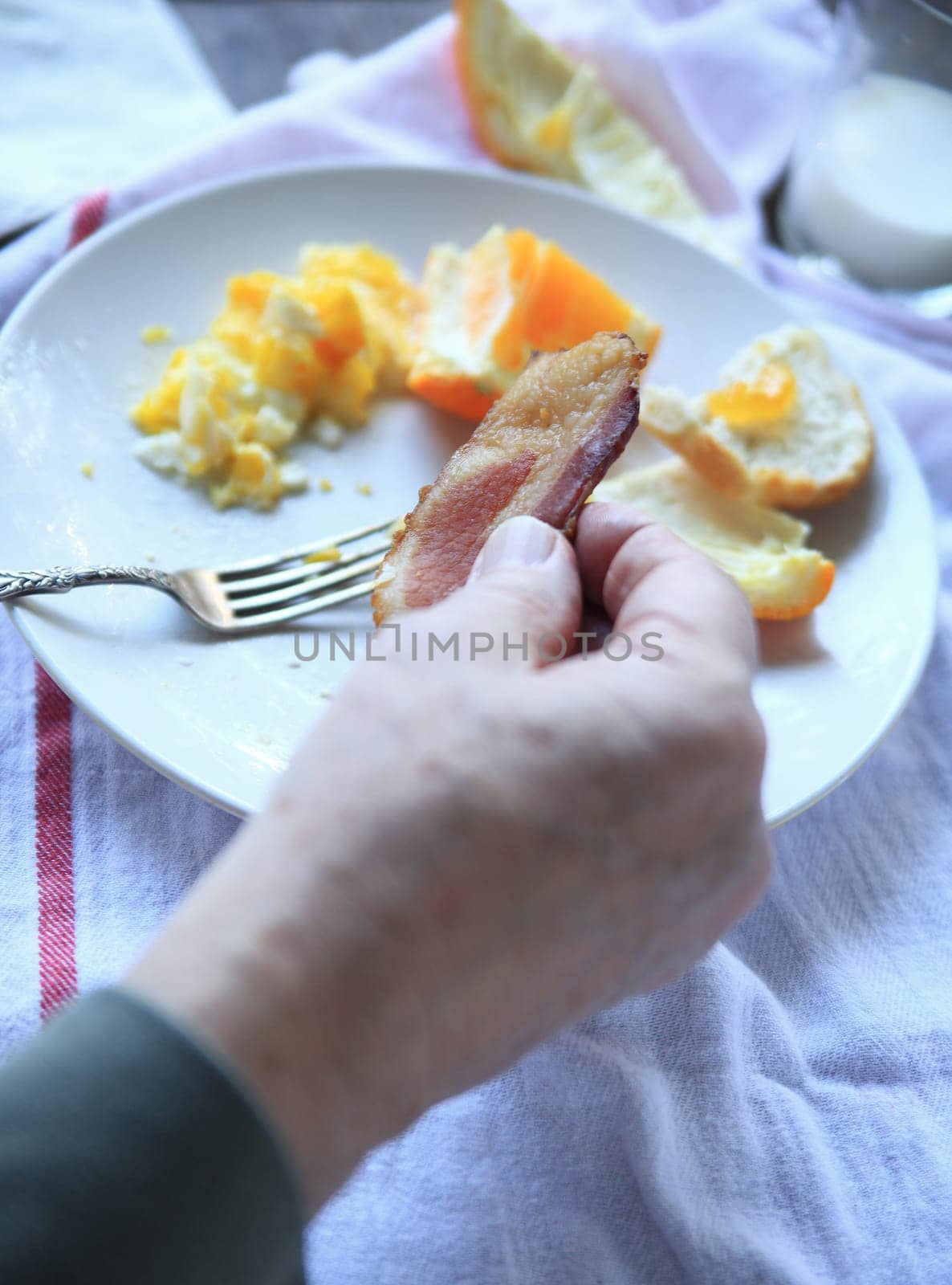 Man with slice of bacon as part of his scrambled egg and fresh fruit breakfast