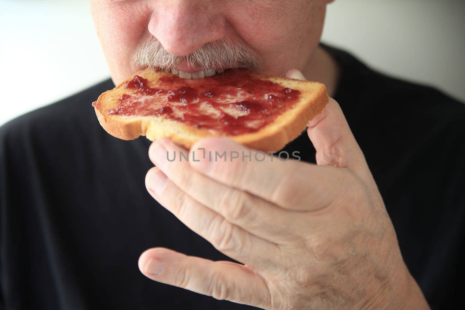 Senor man eating buttered toast spread with grape jam