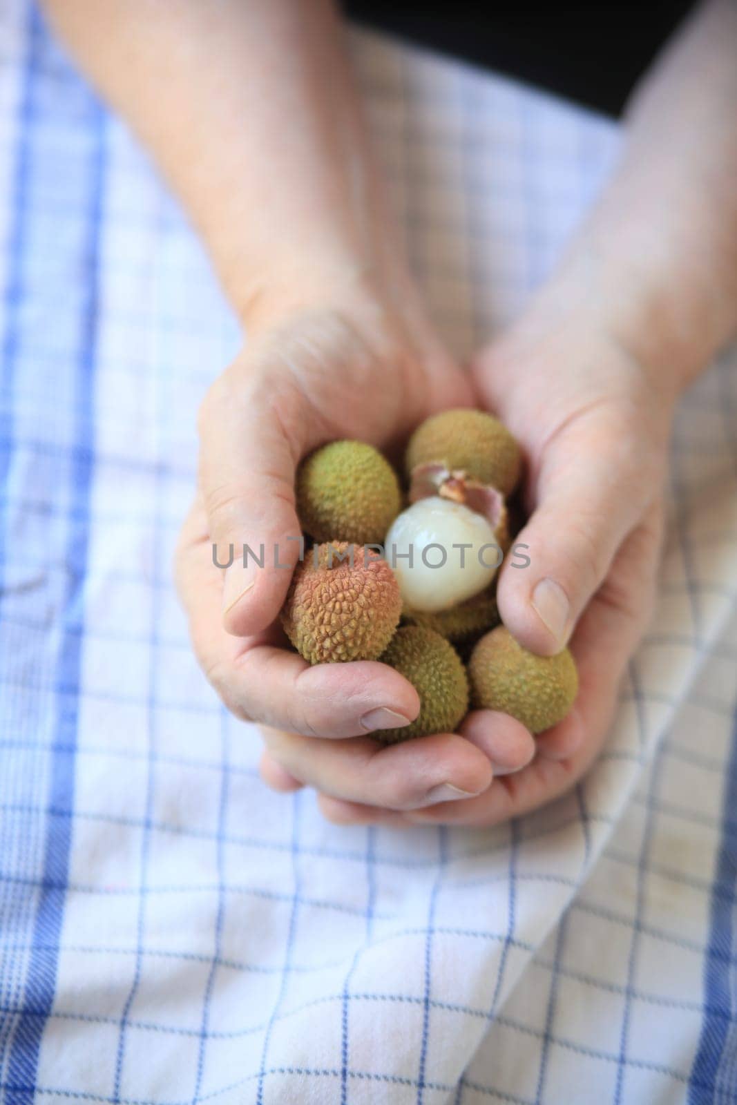 A man holds fresh lychee fruits, one peeled, in his hands.