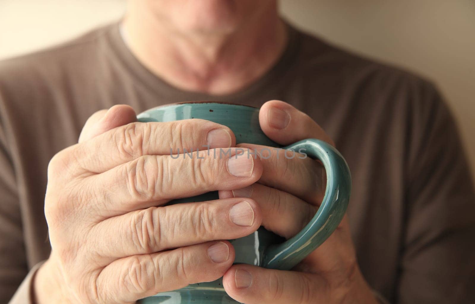 Older man warms his hands with a cup of hot coffee.