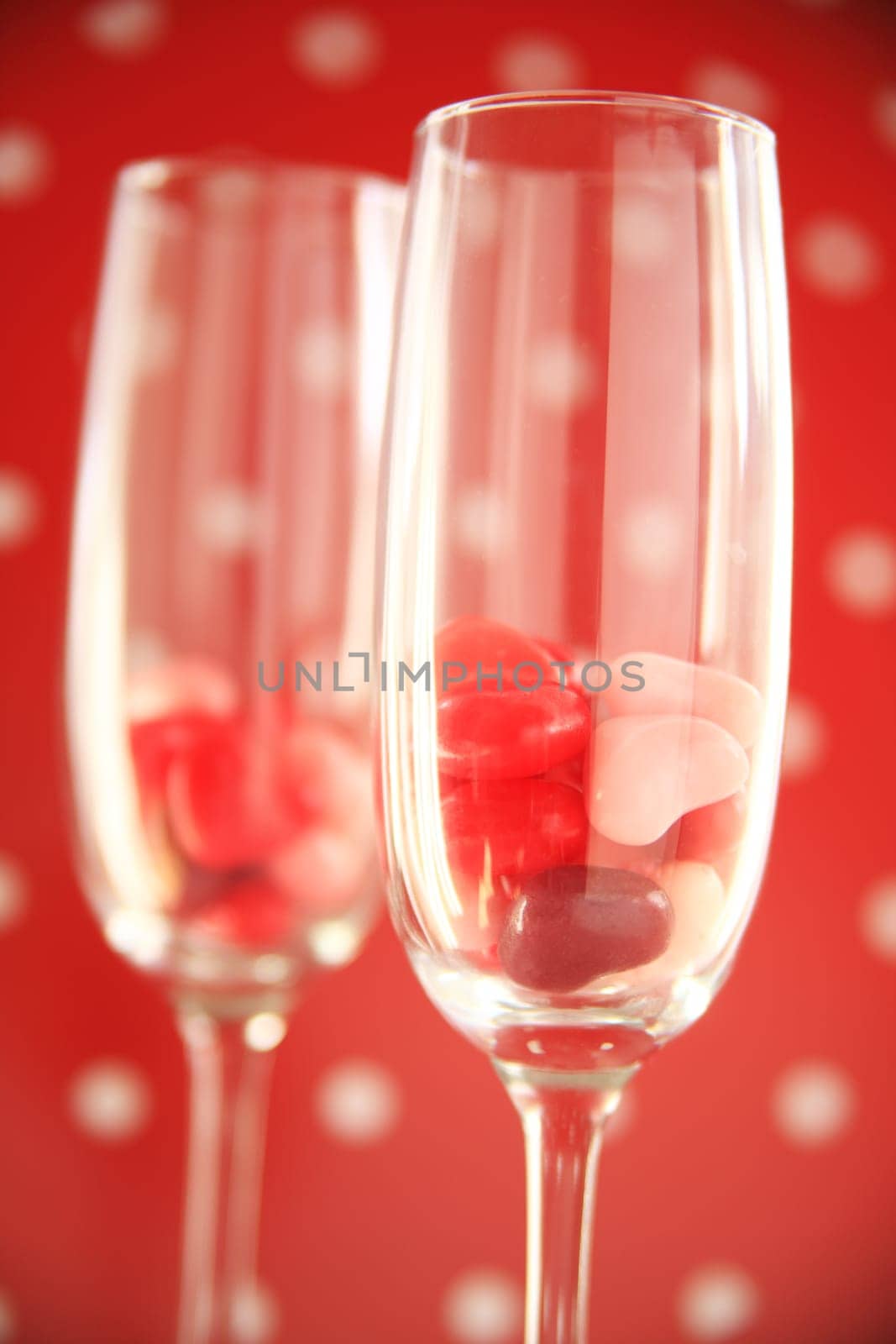 Two wine flutes with candy hearts against a red and white polka dot background