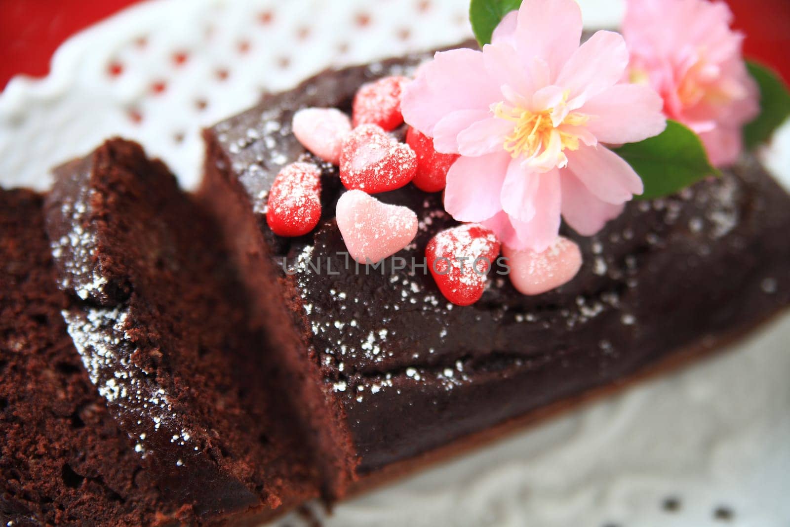 Chocolate loaf cake decorated with powdered sugar, candy hearts and fresh camellias