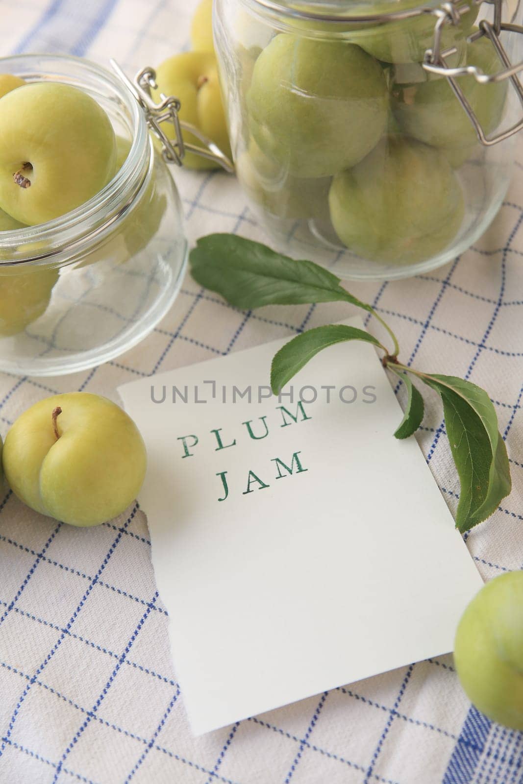 Fresh green plums in glass jars and the words plum jam on paper with copy space