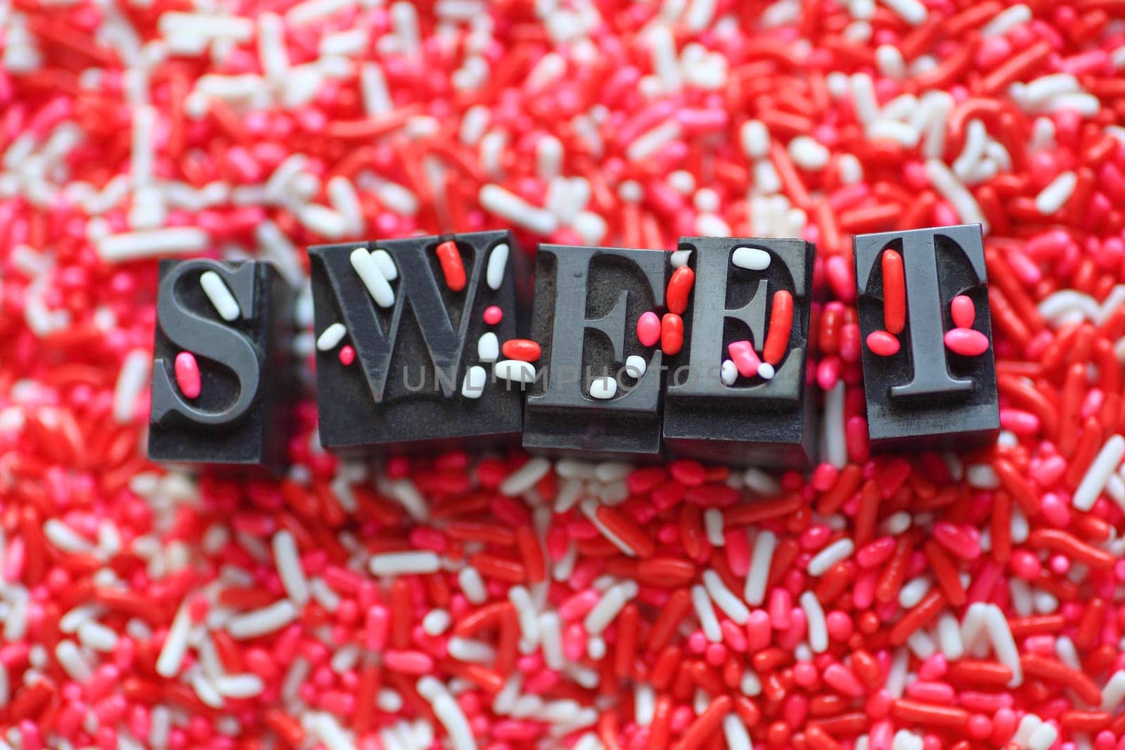The word 'sweet' in metal type on a pink and white candy sprinkles background