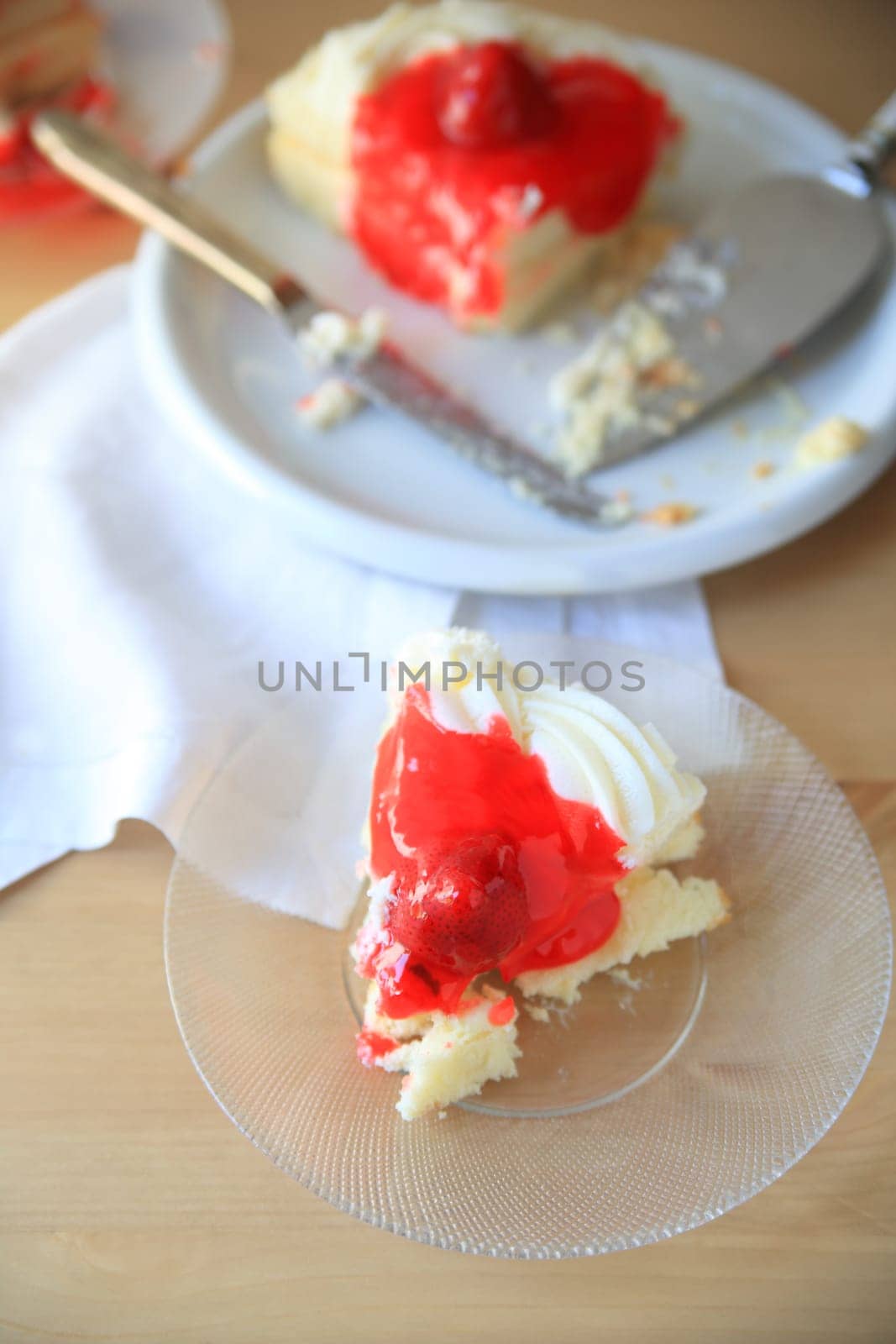 Portion of strawberry-glazed cake on a glass plate,  rest of cake in background