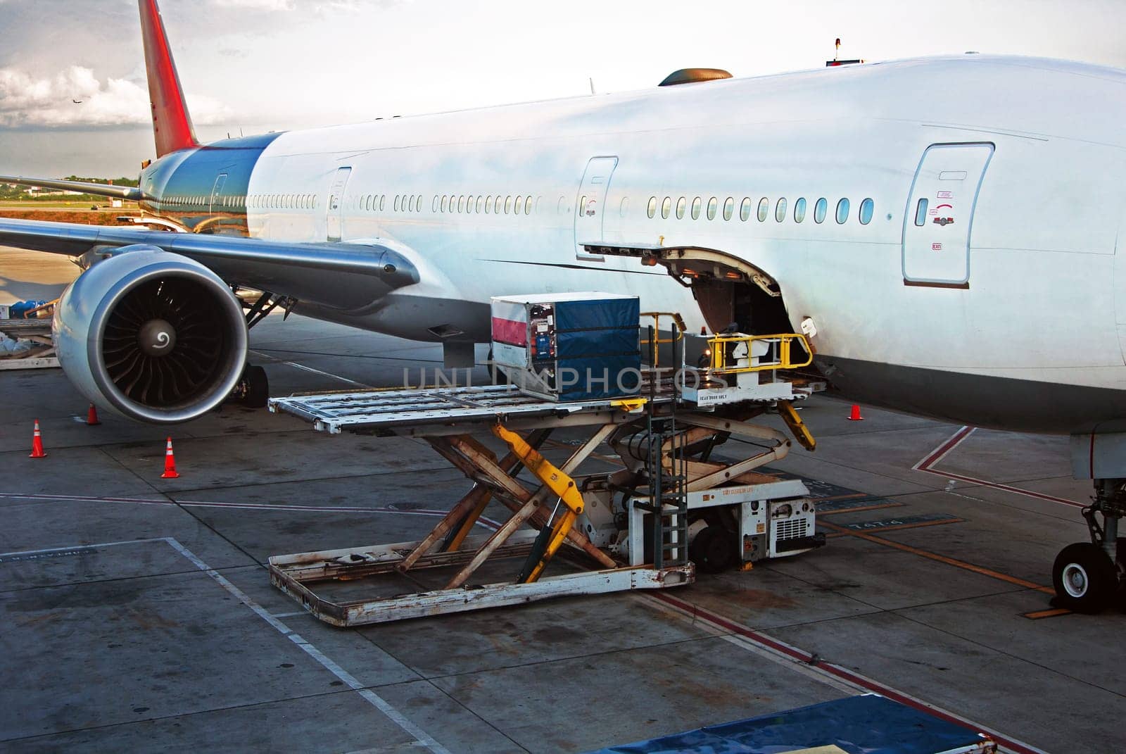 Loading cargo or luggage into airplane at airport on a cloudy day.