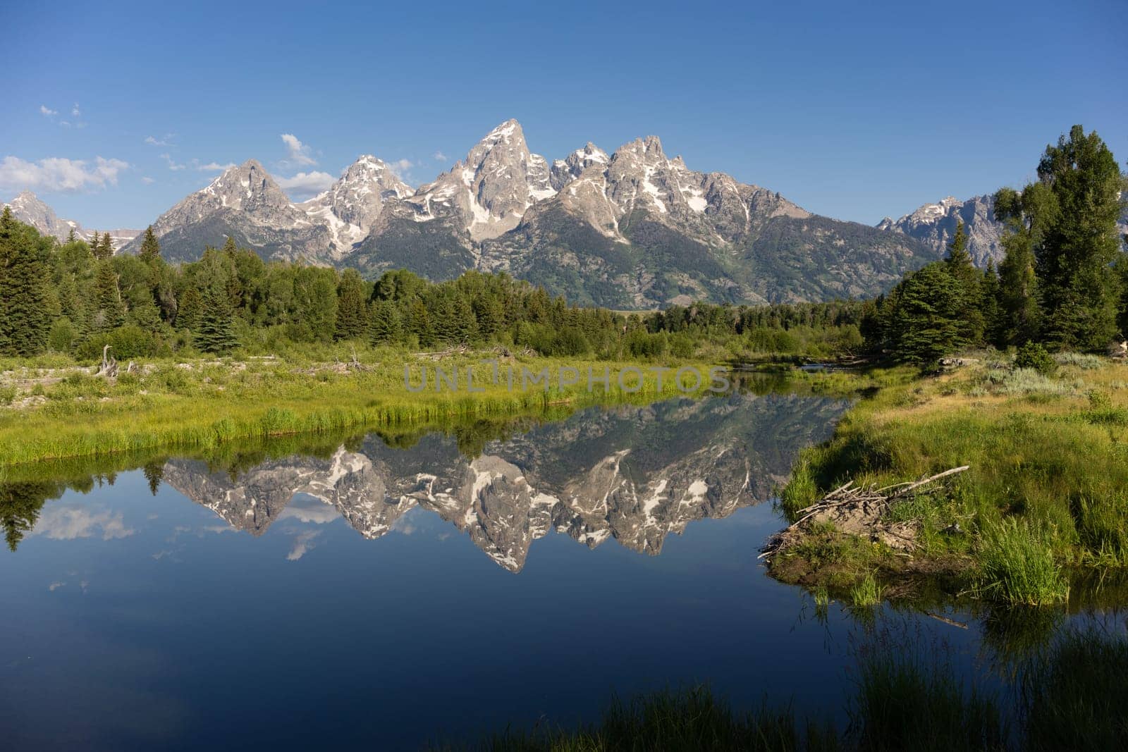 The water is perfectly smooth showing high peak reflections in the Teton's