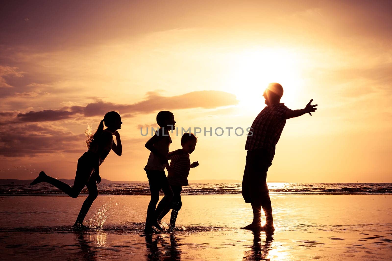Father and children playing on the beach at the sunset time. Concept of friendly family.