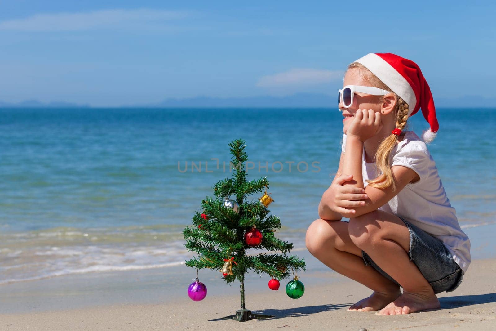 Happy little girl sitting on the beach at the day time. Concept of Happy New Year.