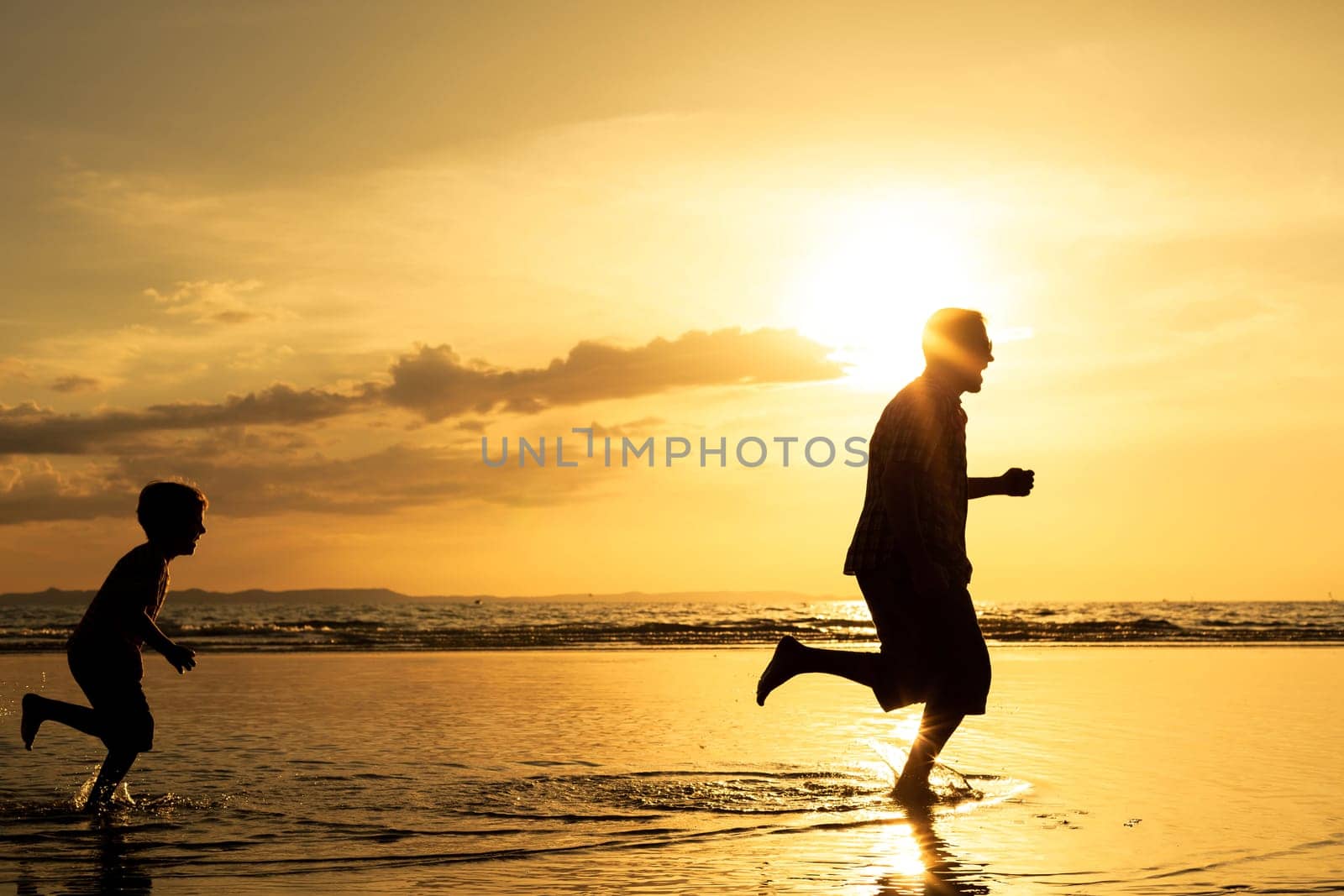 Father and son playing on the beach at the sunset time. Concept of friendly family.