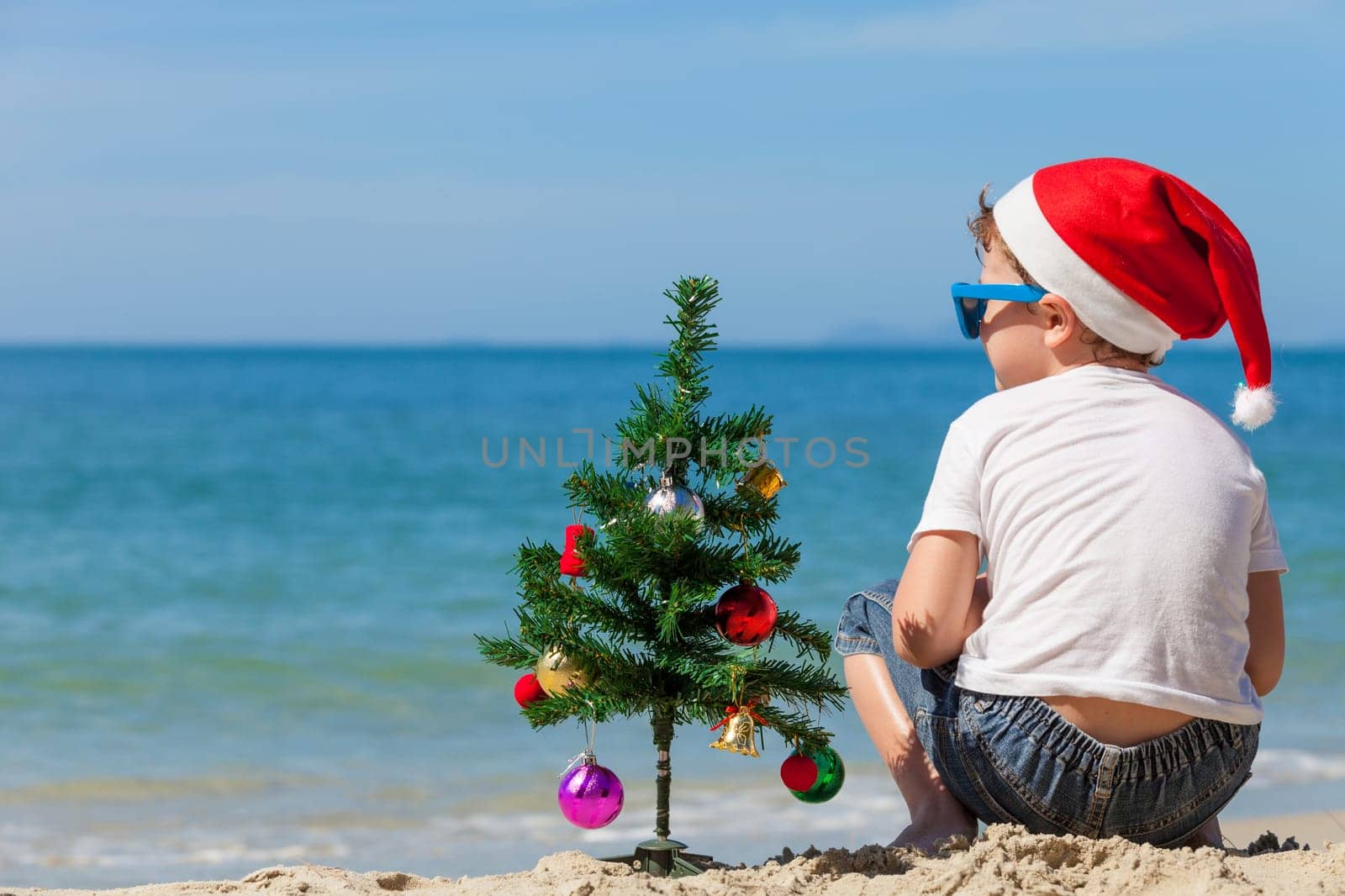 Happy little boy sitting on the beach at the day time. Concept of Happy New Year.