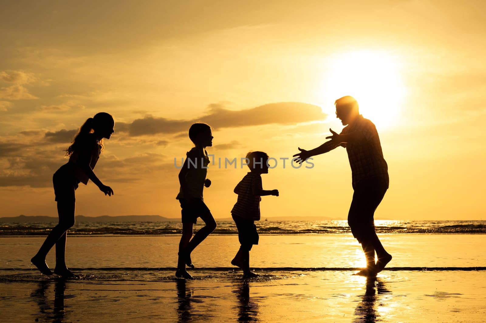 Father and children playing on the beach at the sunset time. Concept of friendly family.