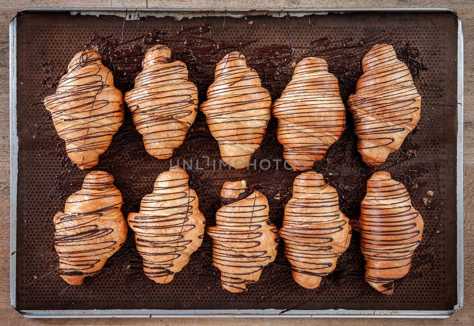 Baked croissant with chocolate placed on brown waxed paper in a stainless steel tray