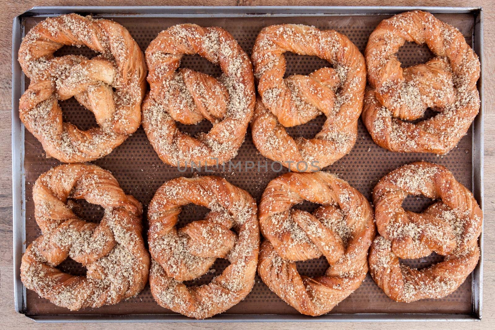 Soft pretzels spread with nuts and sugar holding on brown waxed paper in a stainless steel tray