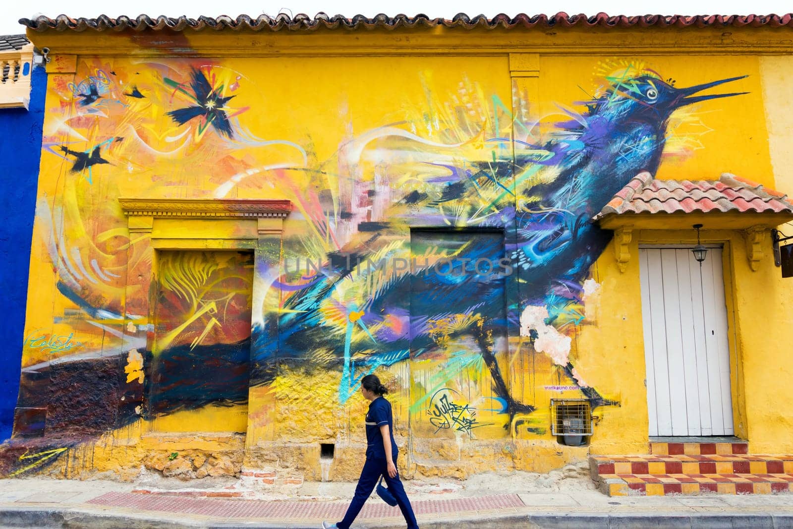 CARTAGENA, COLOMBIA - MAY 24: Woman walking in front of mural on a yellow colonial wall in Cartagena, Colombia on May 24, 2016