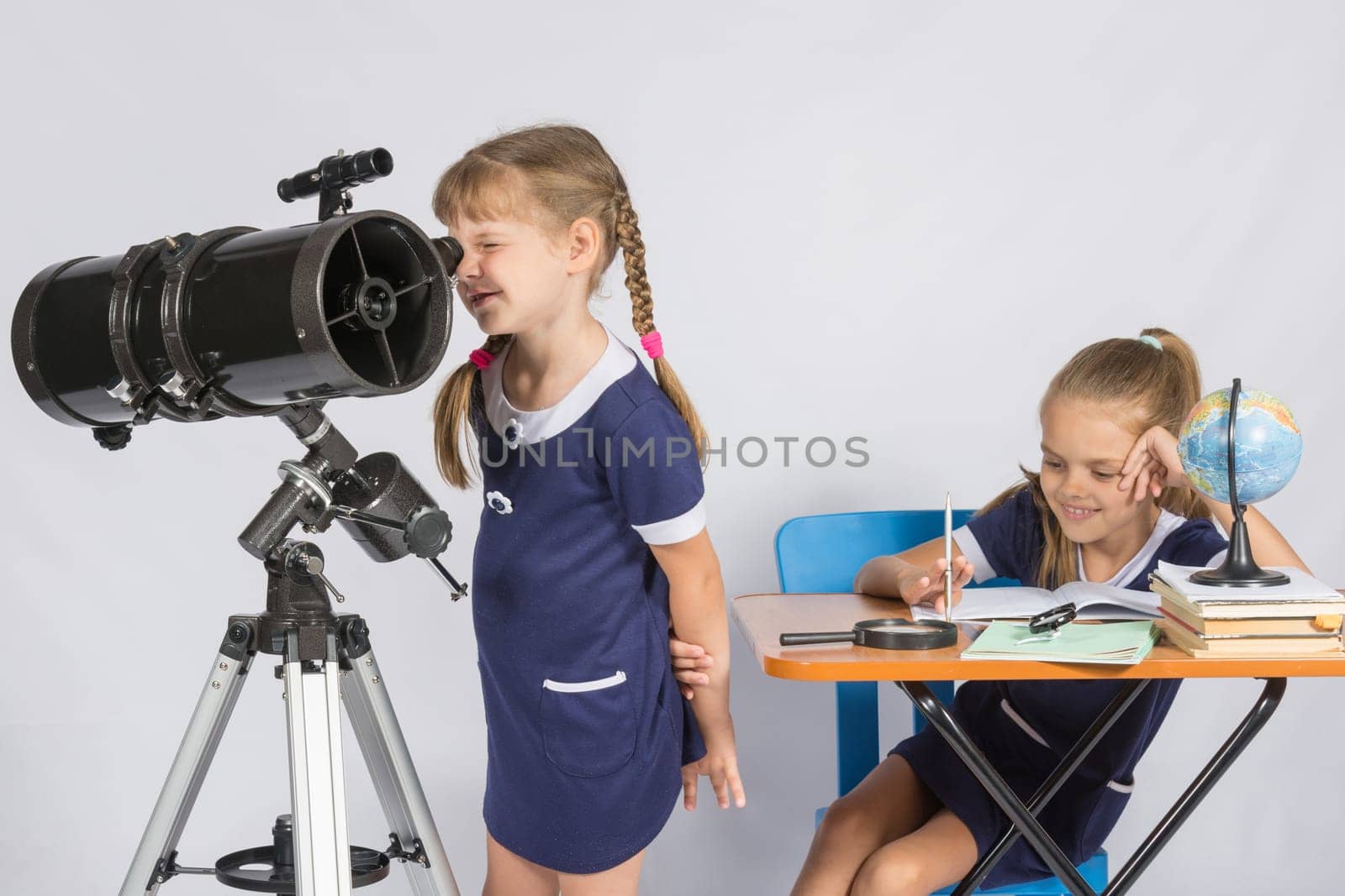 Girl astronomer looks through the eyepiece of the telescope, and the other girl sitting happily at the table