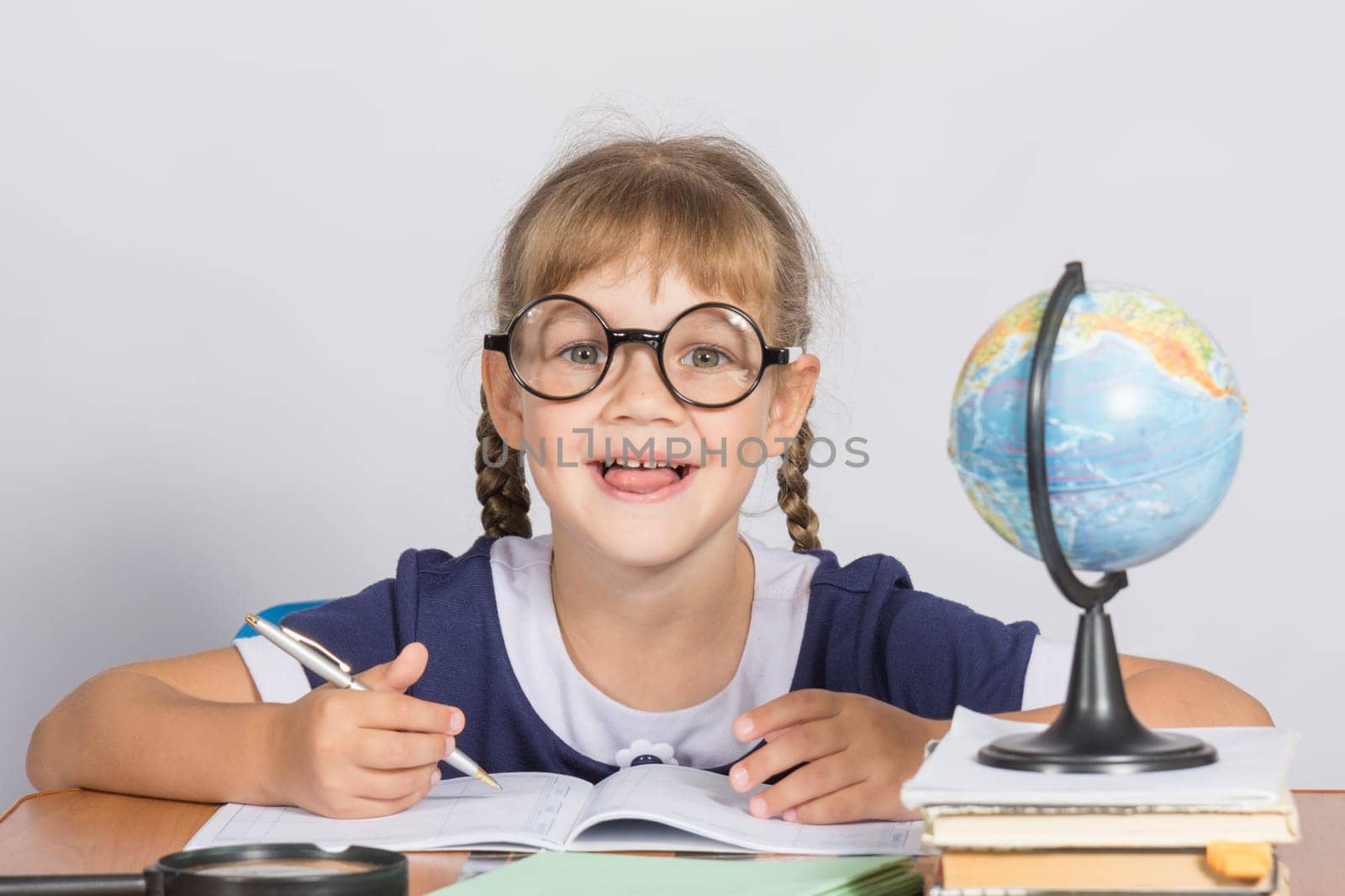 Happy first grader sits at a table in the classroom, with his mouth open in pleasure