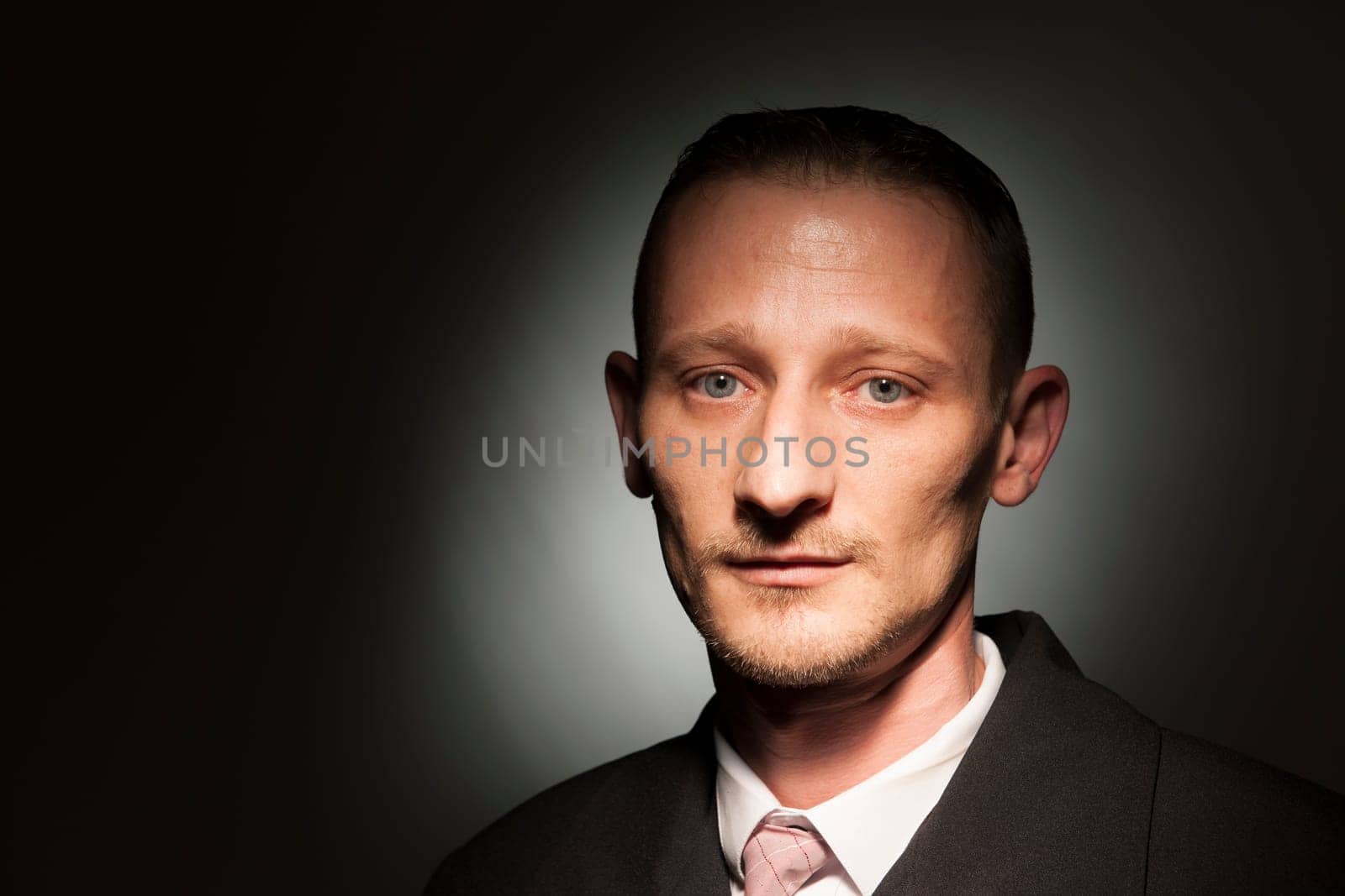 Head-and-shoulder portrait of a middle-aged man in front of a dark studio background with spot light.