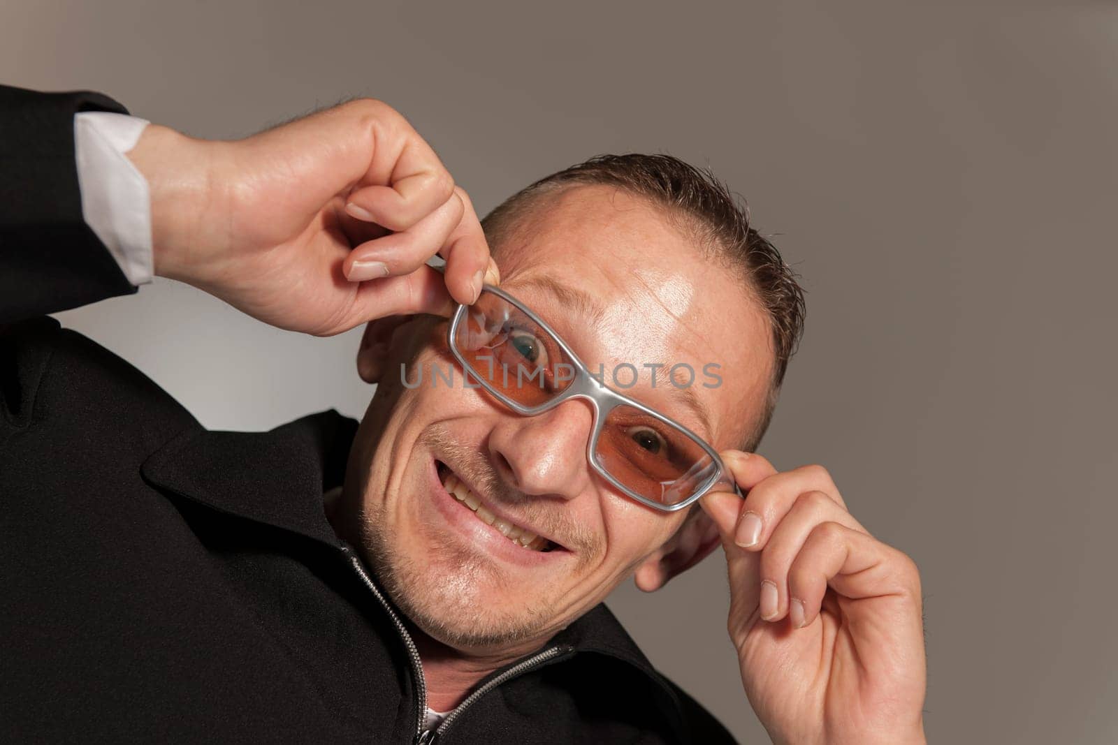 Funny head-and-shoulder portrait of a middle-aged man with sunglasses grimacing against a gray studio background.