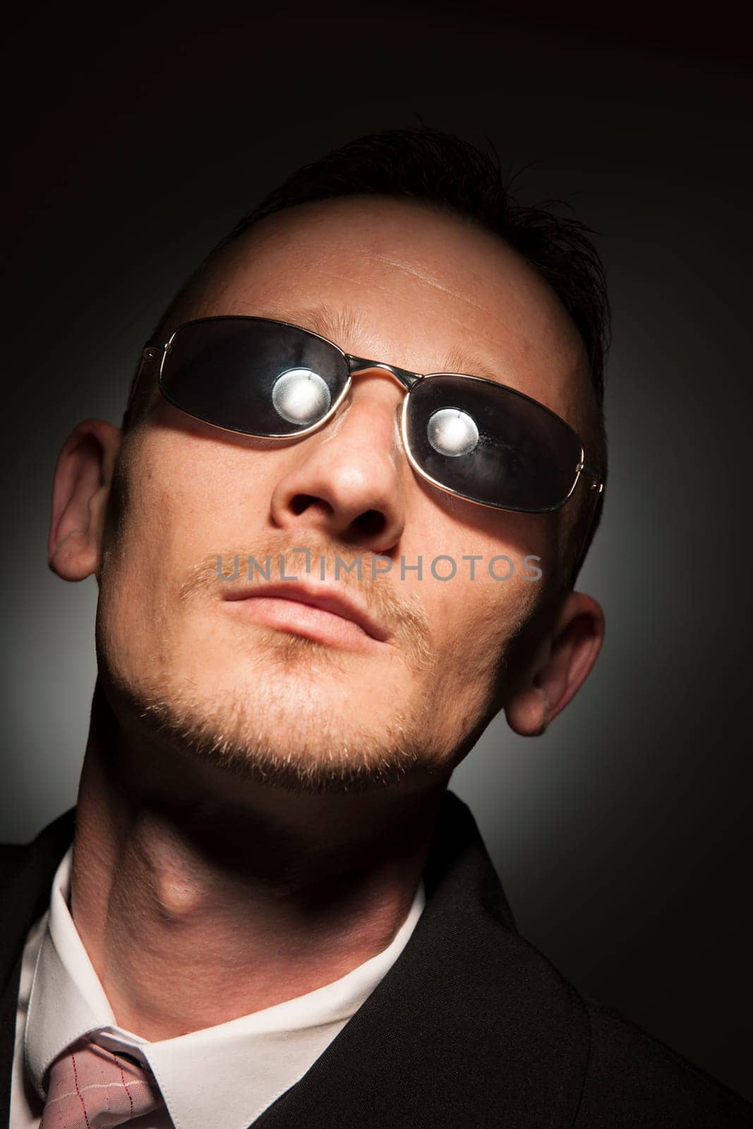 Head-and-shoulder portrait of a middle-aged man with sunglasses in front of a dark studio background with spot light.