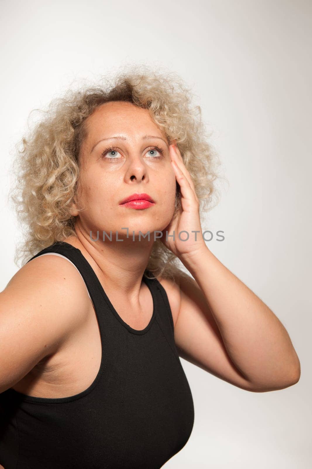 Lateral upper body portrait of a middle-aged blonde woman looking up against a white background posing.