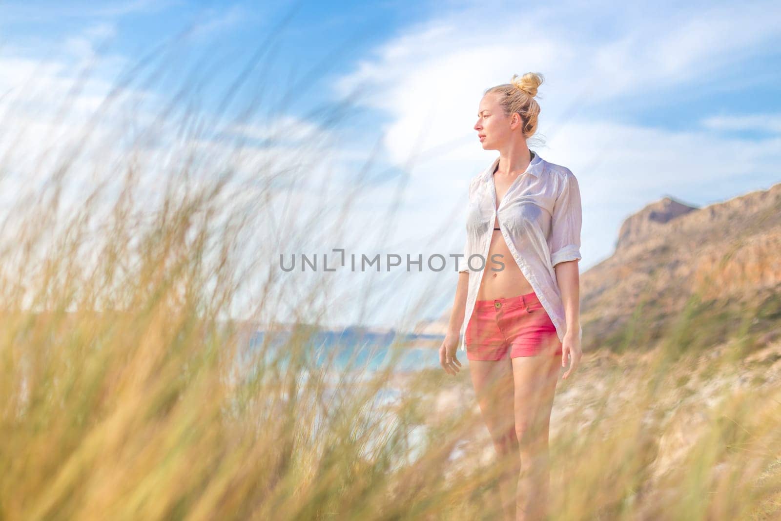 Relaxed woman in white shirt looking at distance, enjoying beautiful nature, freedom and life at serene landscape at Balos beach, Greece. Concept of vacations, freedom, happiness, joy and well being.