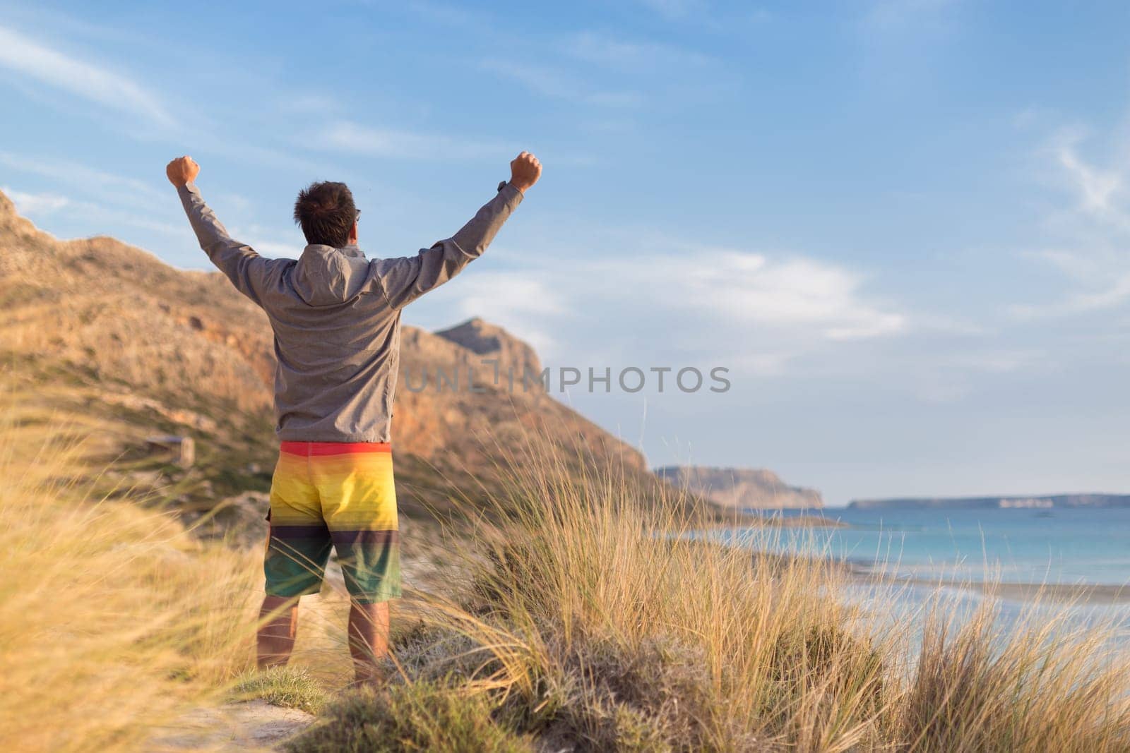 Sporty active man, arms rised, enjoying beauty of nature, freedom and life at beautiful landscape. Active lifestyle outdoors. Made it.