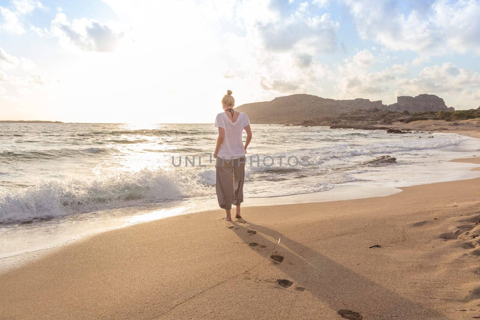 Woman walking on sand beach at golden hour. Seashore sunset walk.