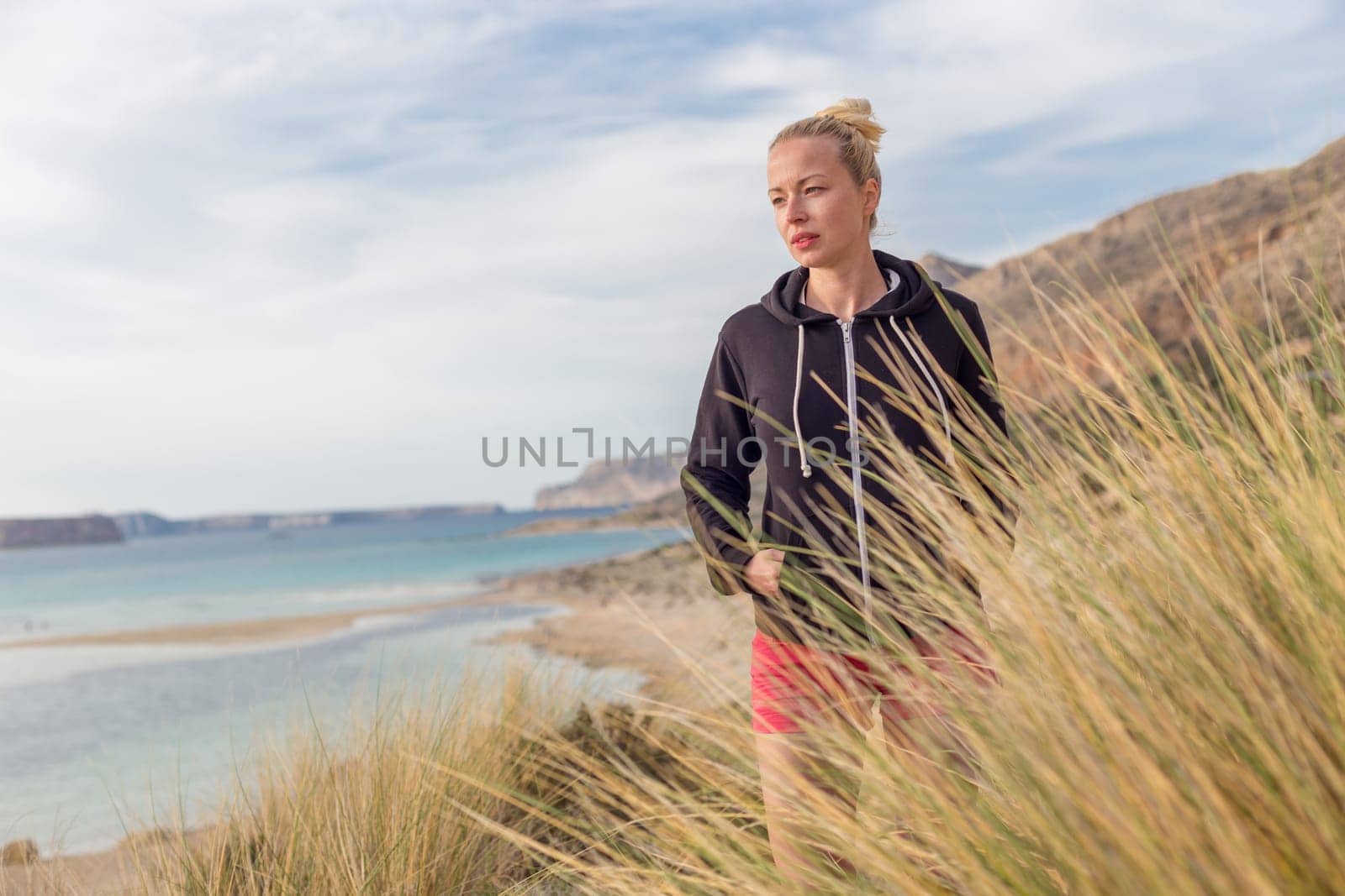 Relaxed woman in dark hoodie walking on serene Balos beach, Greece, enjoying beautiful nature and nice views.