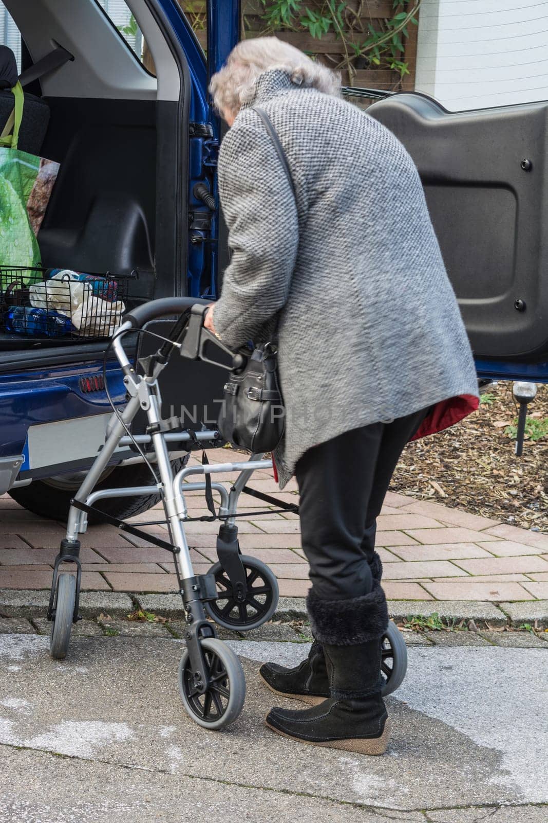 Elderly lady with a rollator in front of a car..