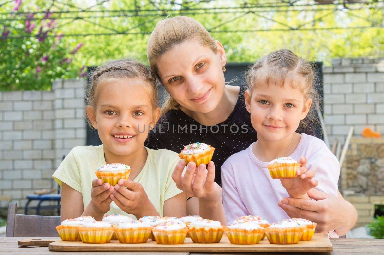 Mother and two daughters sitting at the table with Easter cupcakes in his hands and looked into the frame