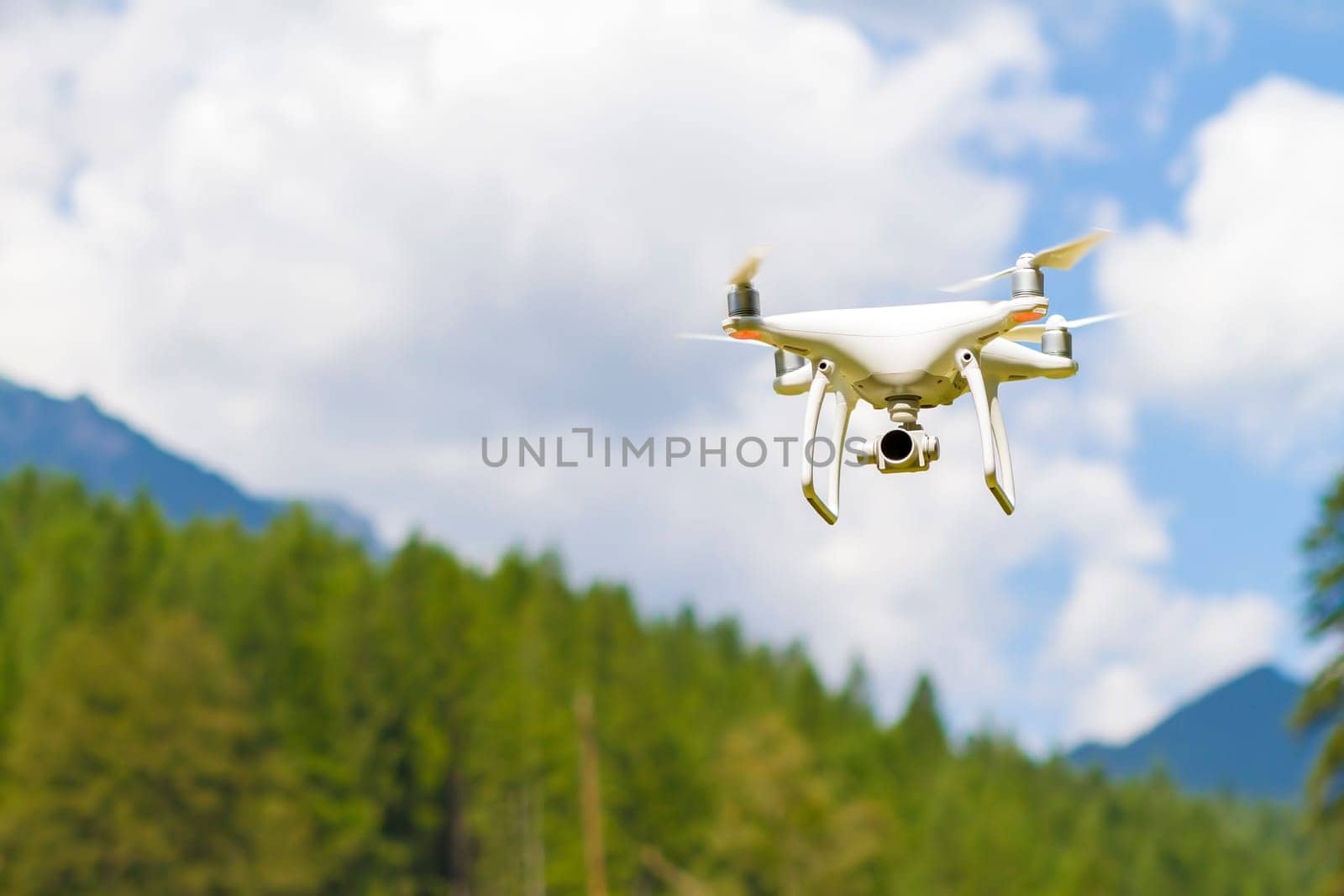 White drone quad copter with high resolution digital camera flying in the blue sky over the mountain.
