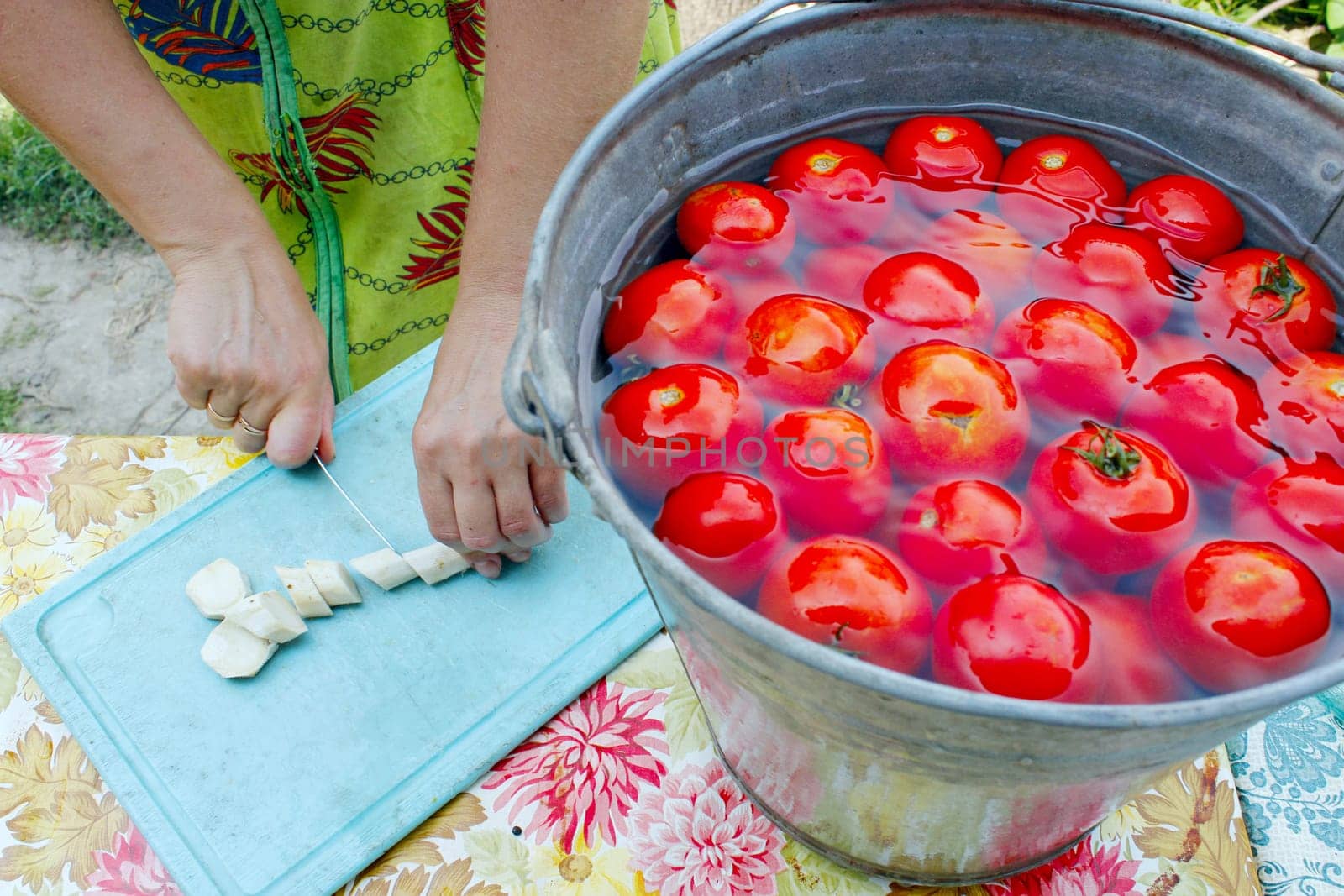 woman slices horseradish for preservation of ripe washed tomatoes in the water