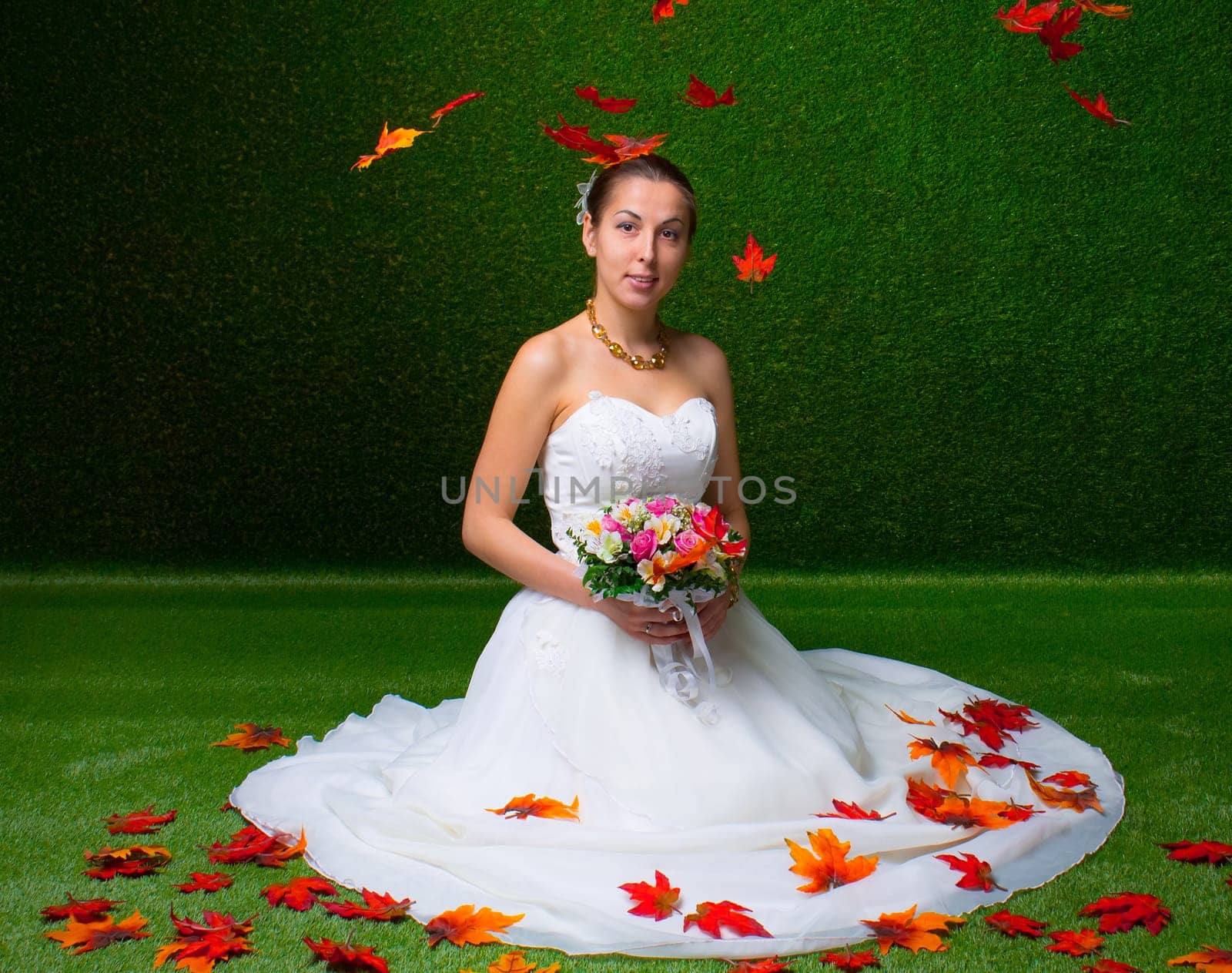 Young and beautiful bride with the flower bouquet and  falling red maple leaf the green background