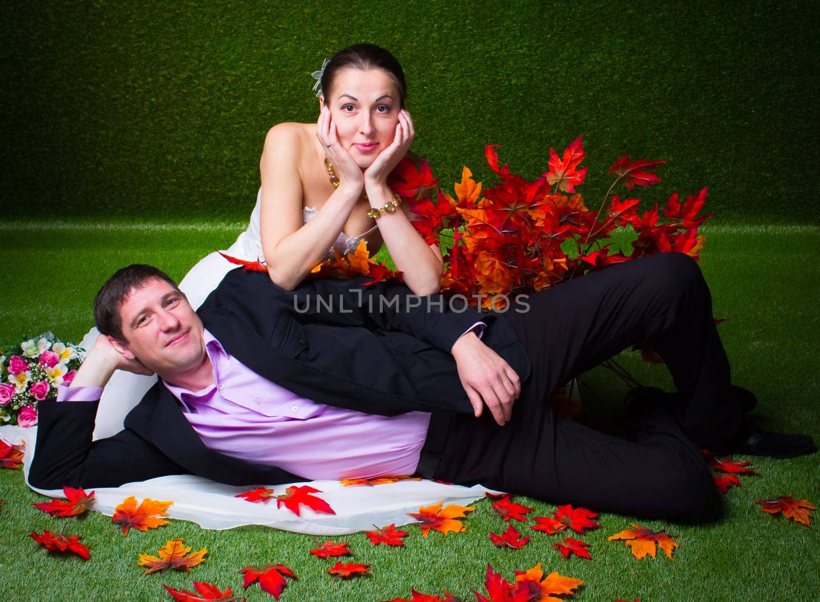 Bride and groom sitting together on a green background and red maple leaf