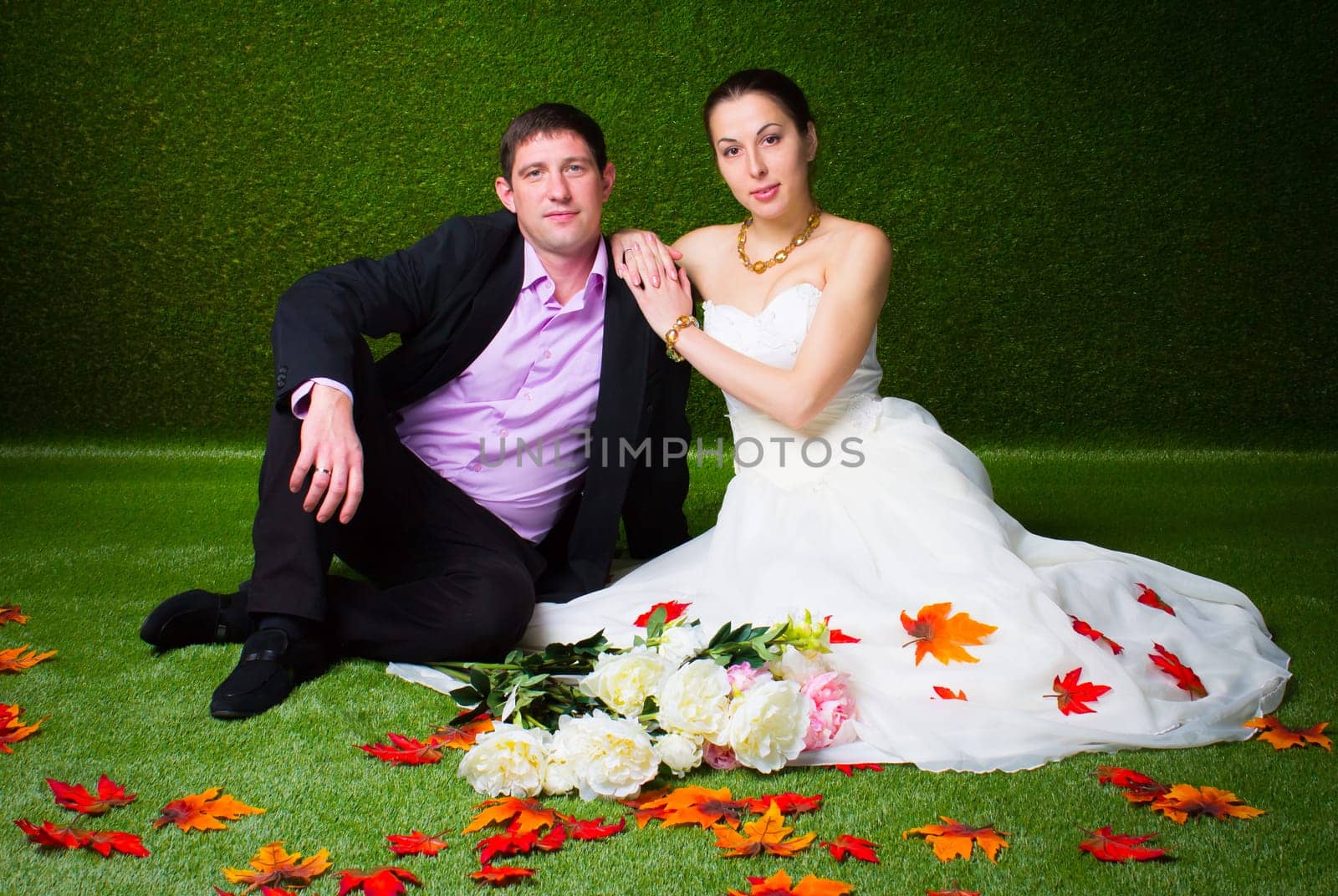 Bride and groom sitting together on a green background and red maple leaf