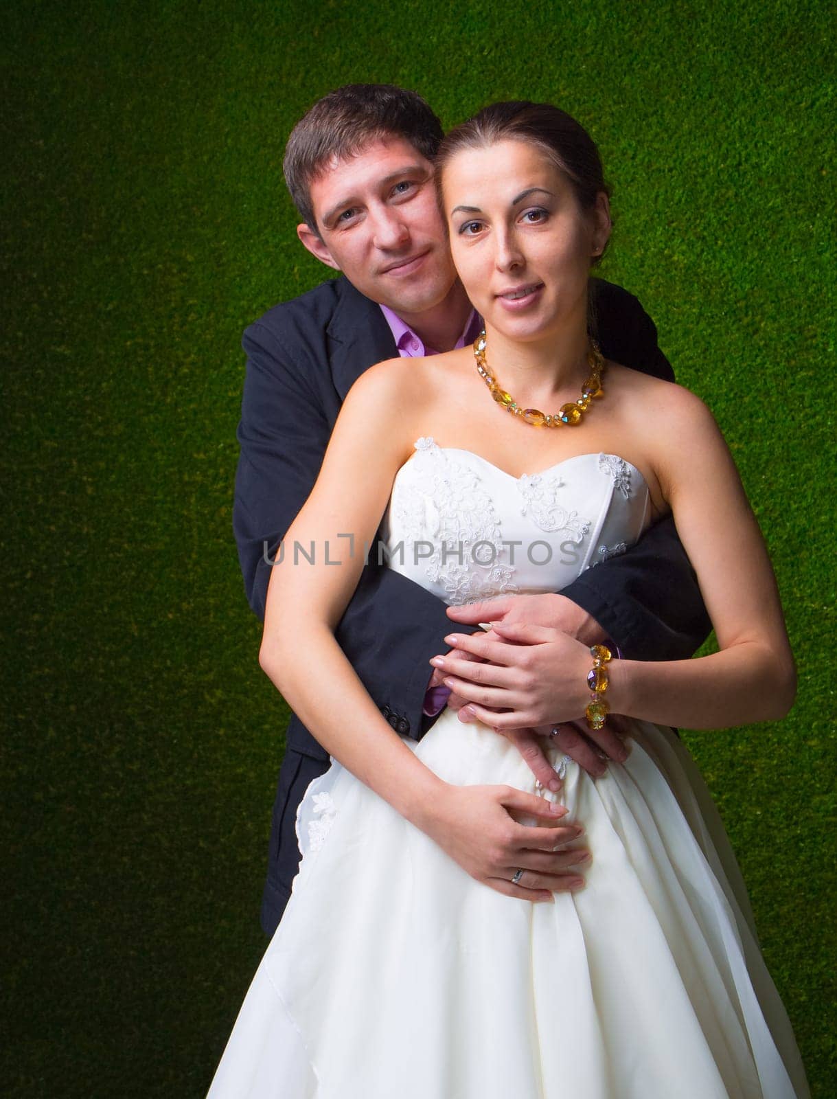 Happy pregnant bride and groom embracing together with stomach unborn child