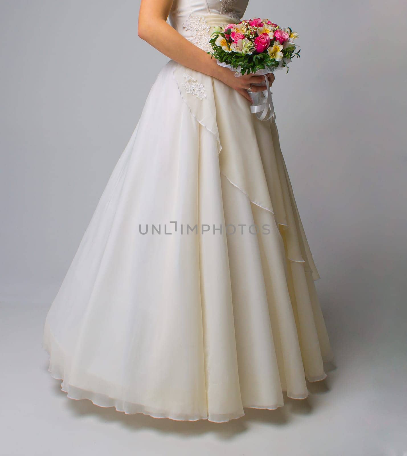 The beautiful bouquet of different colors in the hands of the bride in a white dress