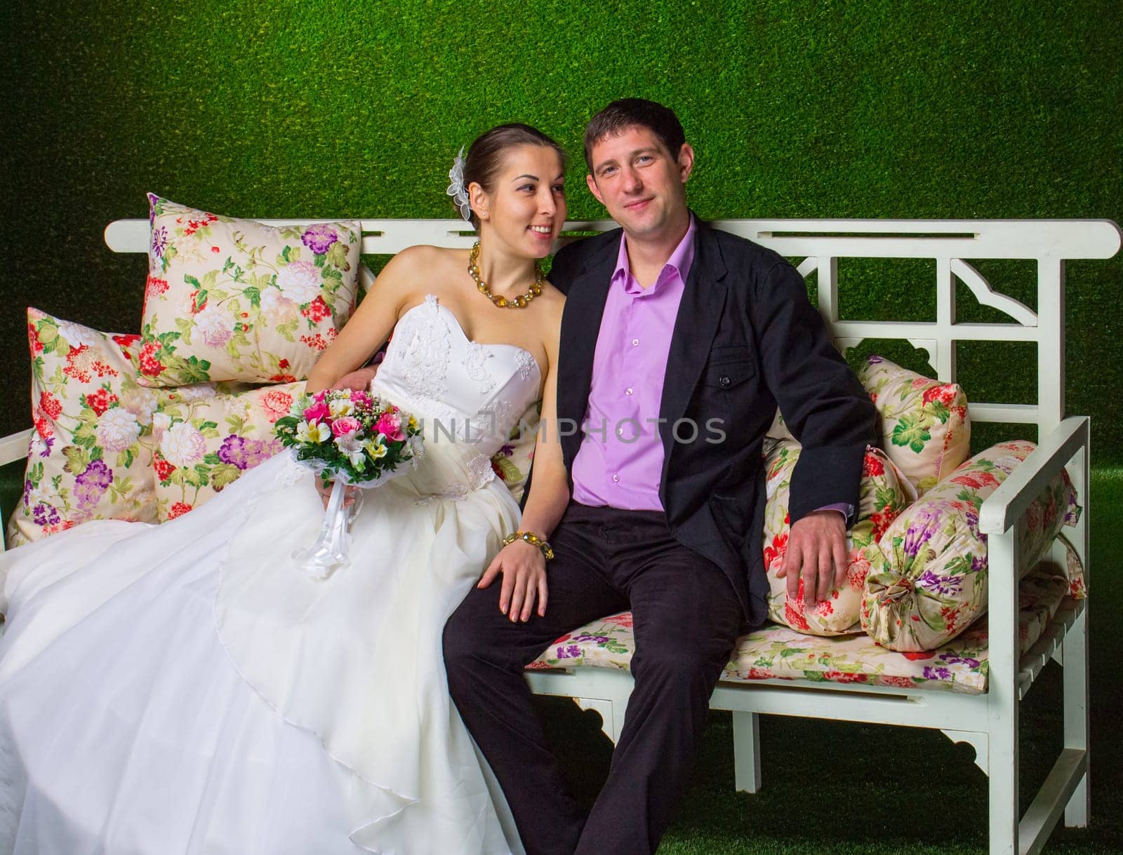 Bride and groom sitting together on a bench on green background