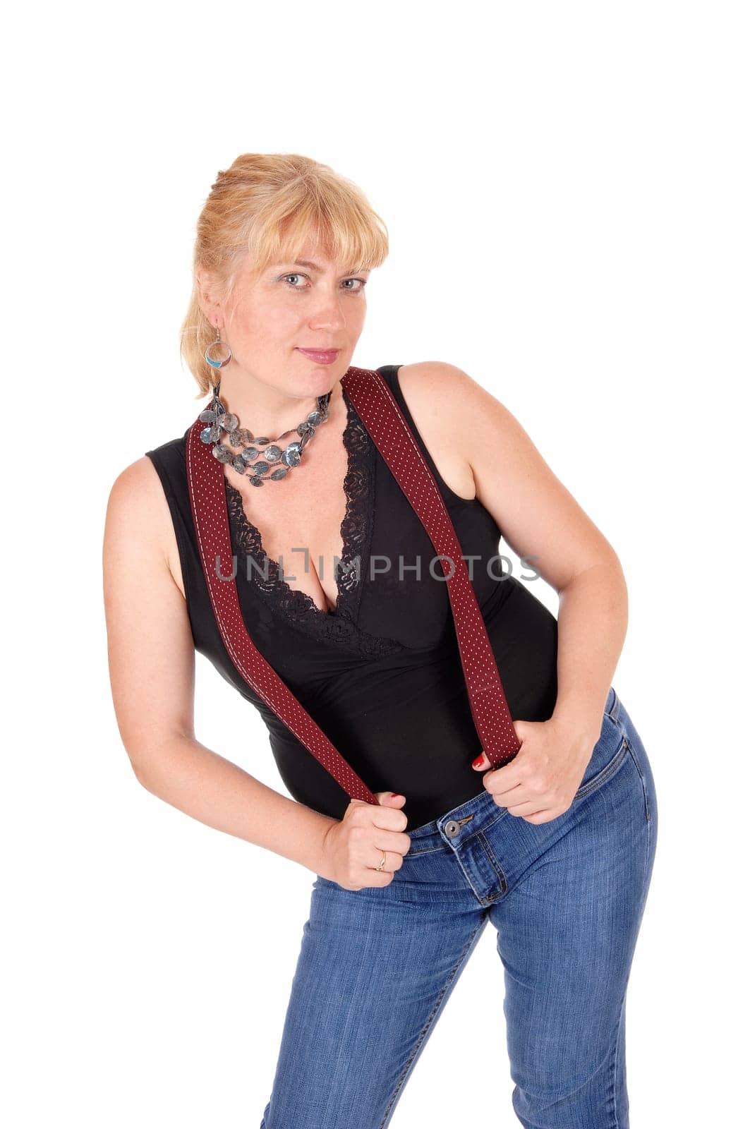 A woman in her forties standing in jeans and a black blouse with red.suspenders and a necklace, isolated for white background..