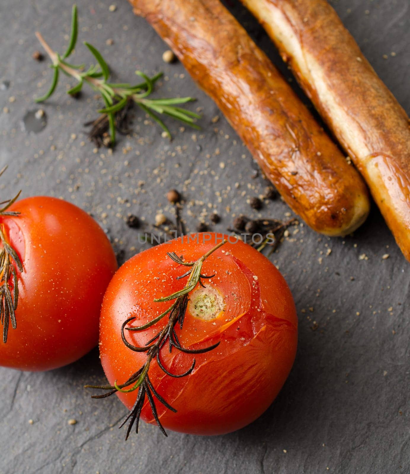 Grilled tomatoes and sausages on a dark slate background