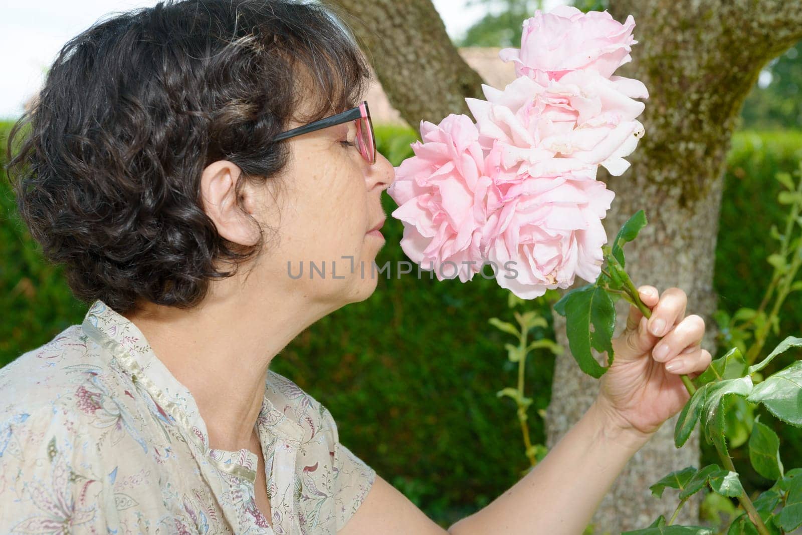a mature woman smelling the rose of her garden