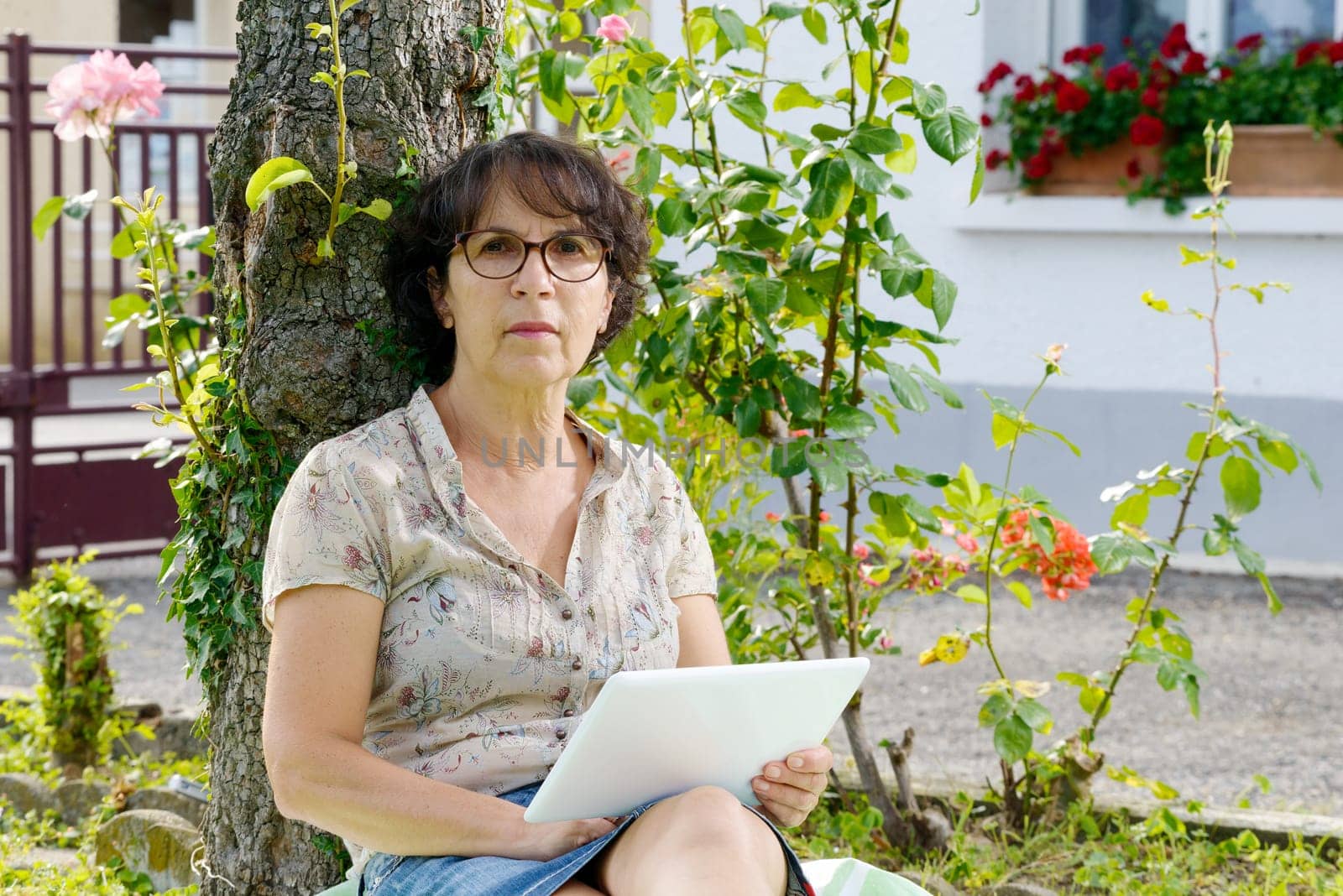 a mature woman sitting with a tablet in the garden