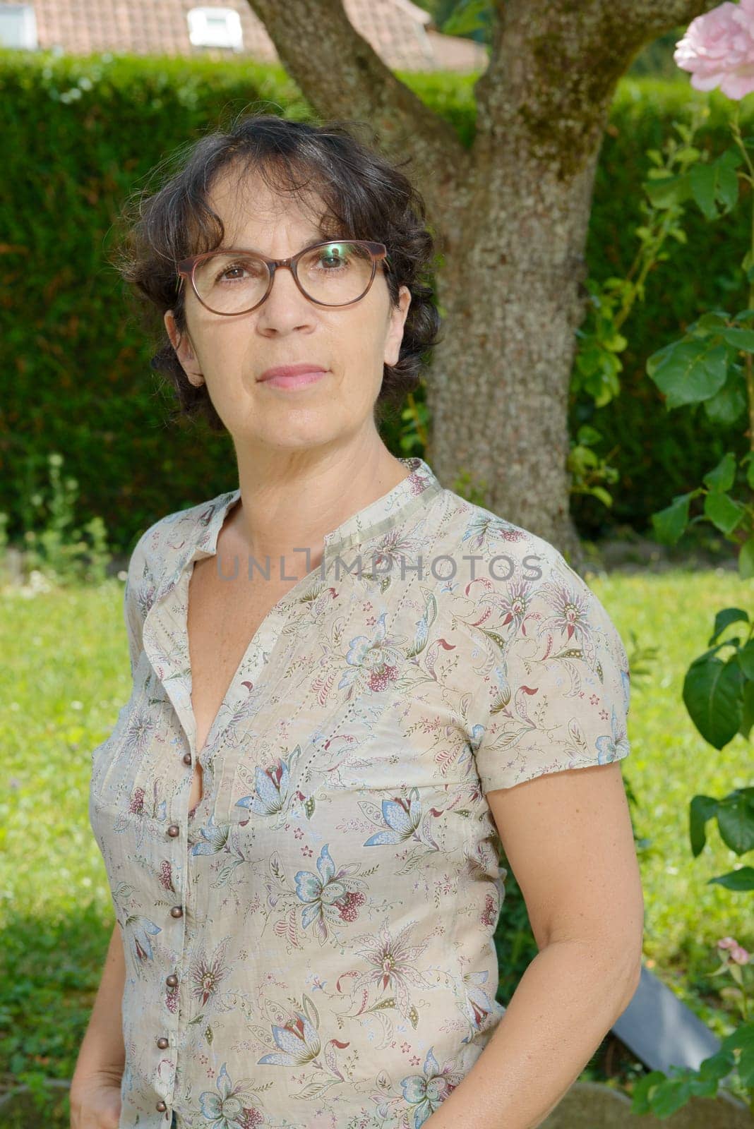 a portrait of a mature woman with glasses in his garden