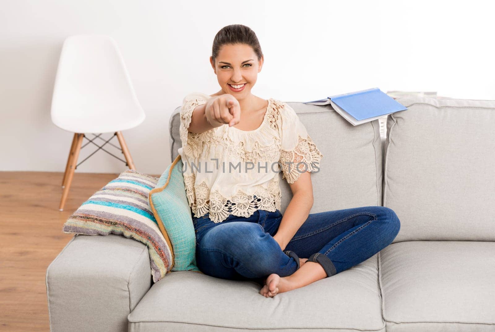 Beautiful woman sitting on the couch and pointing to the camera