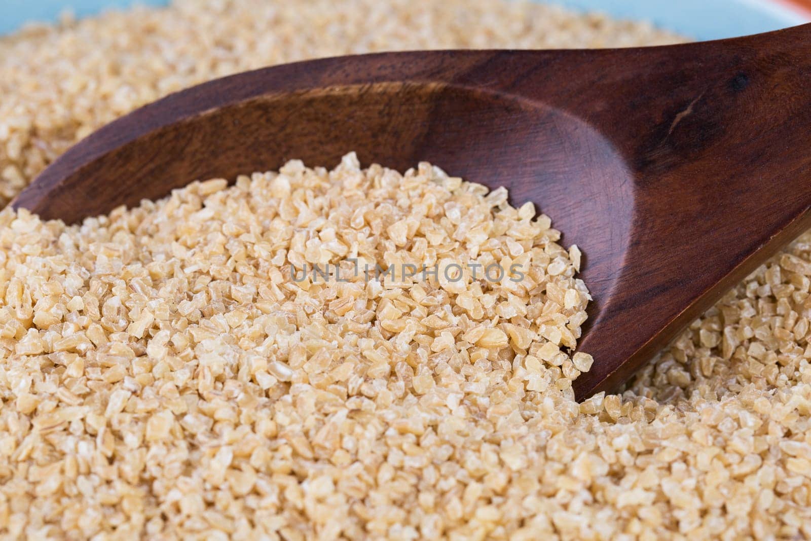 Wooden spoon full of bulgur wheat.