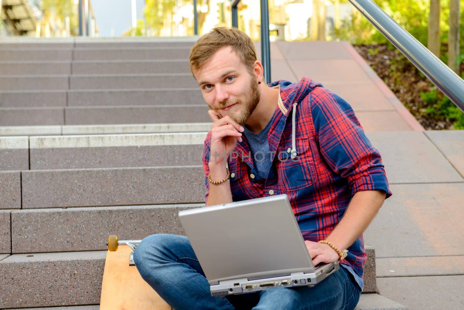 young man in checkered shirt sitting on stairs and using laptop
