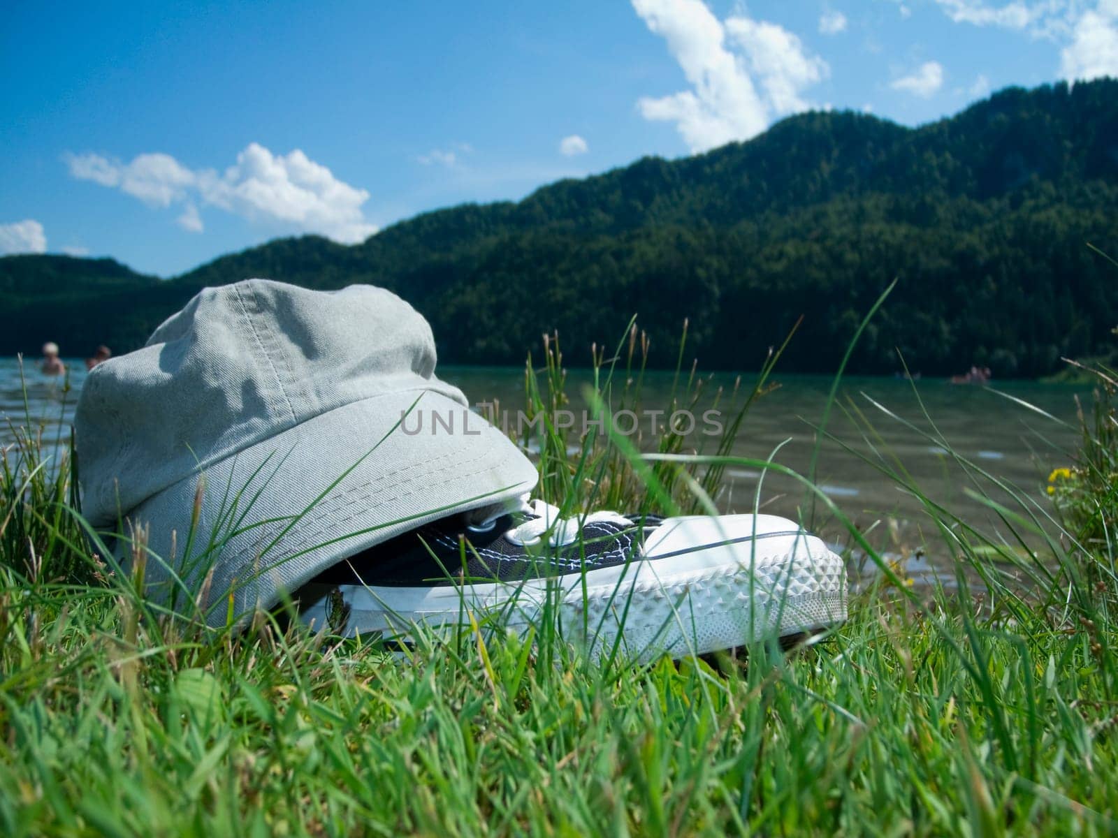 Wide-angle close-up on green grass of fabric sports shoes with a schirmütze placed on it in summer at the Weissensee in the East-Allgäu